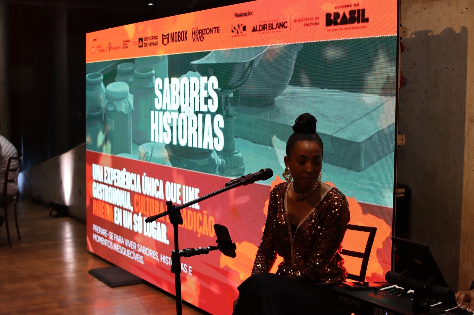 Apresentação musical no palco da Mostra Sabores e Histórias, com o painel do evento ao fundo